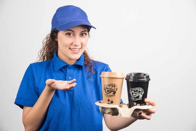 La donna in uniforme blu mostra su due tazze di caffè su priorità bassa bianca