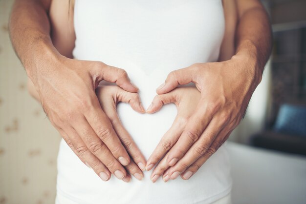 La donna incinta e la sua mano del marito che mostrano il cuore modellano.