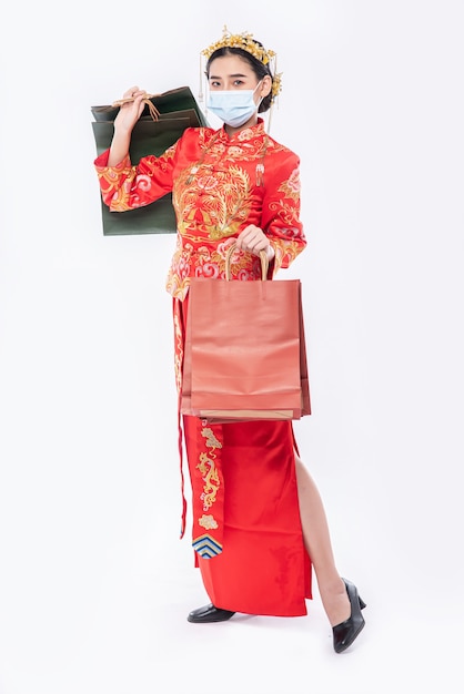 La donna indossa il vestito e la maschera cheongsam tiene il sacchetto di carta dallo shopping nel capodanno cinese