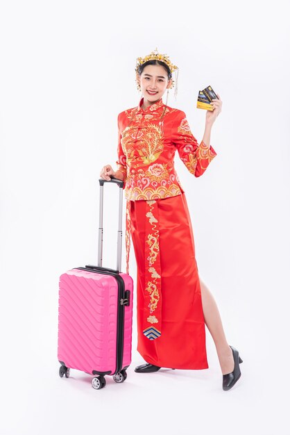 La donna indossa un abito cheongsam con corona prepara la borsa da viaggio rosa e la carta di credito per il viaggio nel capodanno cinese