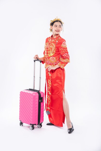 La donna indossa un abito cheongsam con corona pronta per il viaggio con la borsa da viaggio rosa nel capodanno cinese