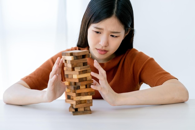 La donna intelligente asiatica di stress di preoccupazione prova a costruire e proteggere il concetto di idee di strategia di gestione del rischio della torre della pila di legno