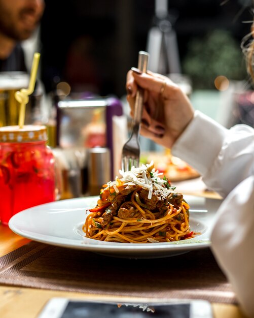 La donna mangia gli spaghetti della pasta con la vista laterale del parmigiano di verdi di carne