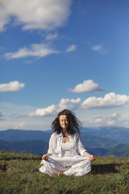 La donna matura sta facendo yoga. Sfondo del cielo di alte cime delle montagne.