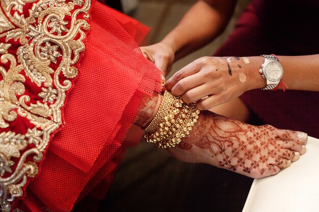 La donna mette il braccialetto d&#39;oro con campane sulla gamba della sposa dipinte