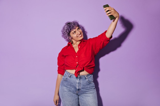 La donna moderna con i capelli viola corti in camicia luminosa prende selfie. Bella donna in abito elegante fa foto.