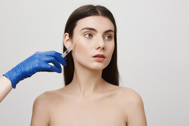 La donna nel salone di bellezza distoglie lo sguardo, riceve l'iniezione del viso di bottox con la siringa