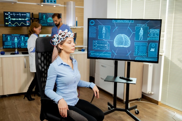 La donna paziente con il dispositivo di scansione della testa e l'attività cerebrale è visibile sullo schermo. Apparecchiature per la diagnosi neurologica