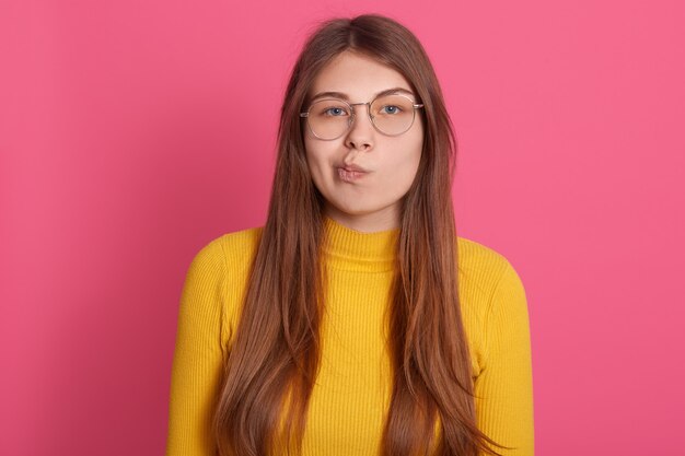 La donna pensierosa sembra triste e seria, ha la bocca contorta, sembra in posa contro il muro rosa, ha bei capelli lunghi e lisci