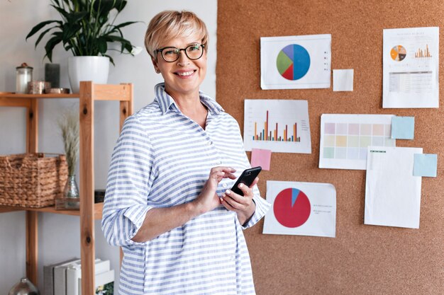 La donna positiva di affari in camicia a strisce tiene lo smartphone