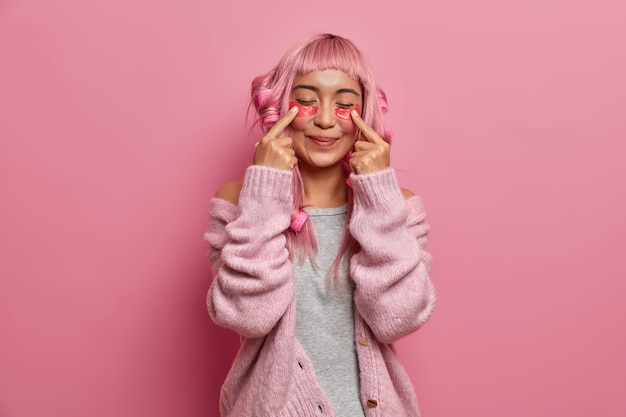 La donna positiva e soddisfatta ha lunghi capelli rosei, acconciatura riccia con bigodini, indica ai cerotti di bellezza, sta con gli occhi chiusi indossa un maglione caldo