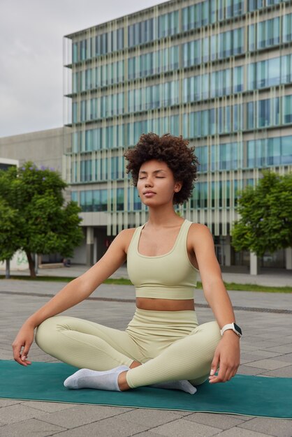 la donna pratica le pose della lezione di yoga con il gesto di mudra sul tappetino di gomma vestito in tuta da ginnastica essendo in un luogo urbano