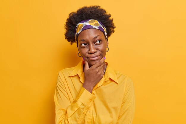 la donna riflette sulla decisione tiene il mento concentrato lontano vestito con una camicia casual pensa a come risolvere il problema pone contro il giallo vivido