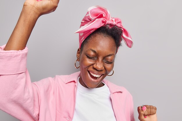 la donna si diverte alla festa tiene le braccia alzate danze alla musica gode di piacevoli momenti di eventi vestita con abiti alla moda isolati su studio grigio