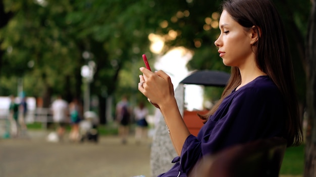 La donna si siede in panchina e utilizzando smartphone. Vista ravvicinata