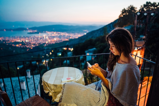 La donna si siede sul balcone, sullo sfondo la città di notte