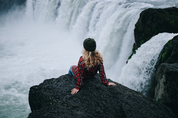 La donna si siede sul bordo della scogliera sulla cascata