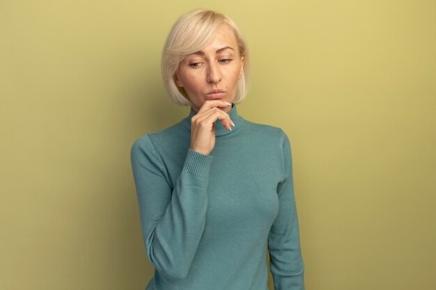 La donna slava abbastanza bionda premurosa tiene il mento e guarda giù isolato sulla parete verde oliva