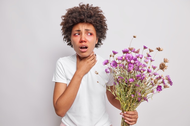 la donna soffoca ha una reazione allergica sui fiori di campo tiene la mano sulla gola ha difficoltà a respirare gli occhi rossi pruriginosi indossa una maglietta casual isolata su bianco
