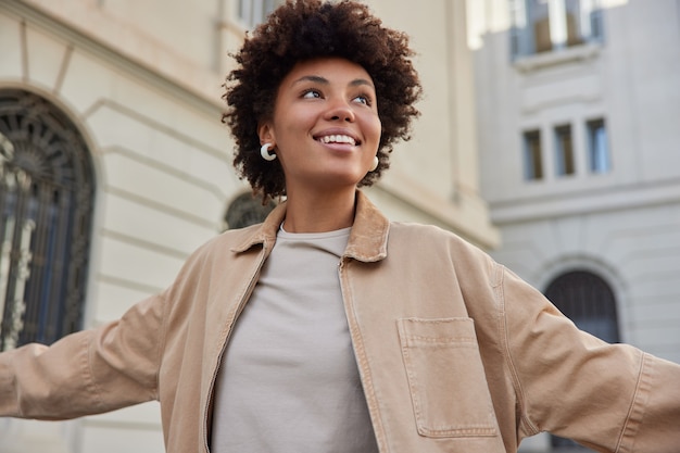 la donna sorride positivamente si sente libera vestita con una giacca beige ha un'espressione felice passeggiate nella città antica gode di un'escursione