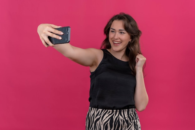 La donna sorridente che indossa la maglietta nera prende un selfie sulla parete rosa