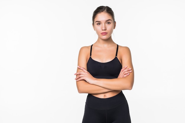 La donna sorridente di sport che sta con le armi ha piegato e che esamina la macchina fotografica isolata sulla parete bianca