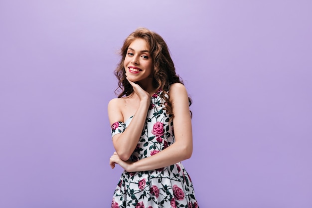 La donna sorridente in vestito grazioso posa su priorità bassa isolata. Bella signora con labbra rosse e capelli lunghi ricci che esamina la macchina fotografica.