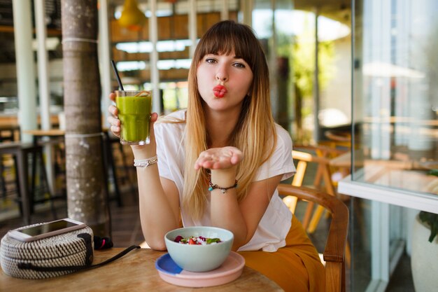 La donna sorridente romantica invia il bacio e mangia la prima colazione sana del vegano.