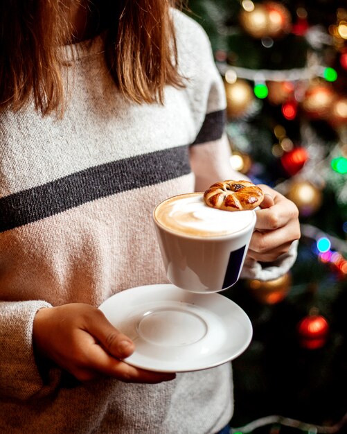 La donna tiene una tazza di cappuccino con biscotto su di esso