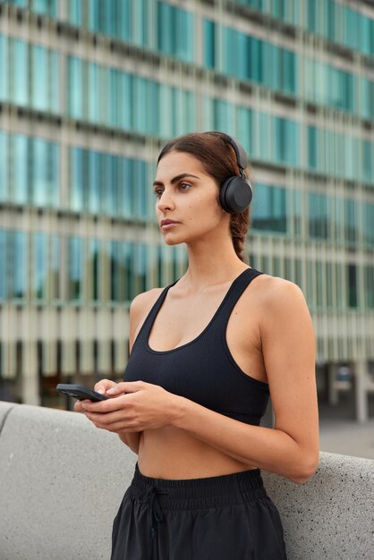 la donna usa il telefono cellulare per la comunicazione online ascolta la musica nelle cuffie sceglie la traccia audio per l'allenamento focalizzato sulla distanza indossa abiti sportivi