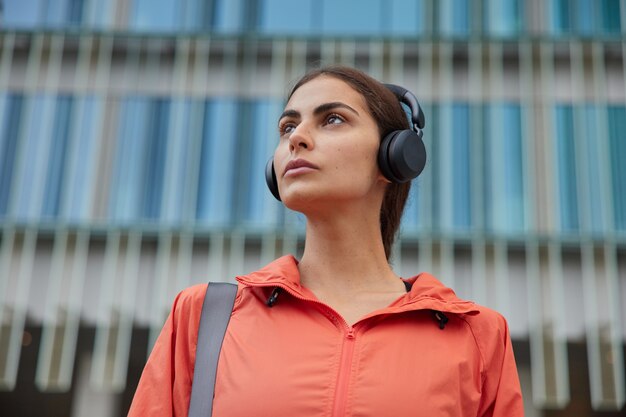 la donna utilizza le moderne tecnologie durante l'allenamento sportivo focalizzato da qualche parte ascolta musica con le cuffie pone contro un edificio moderno