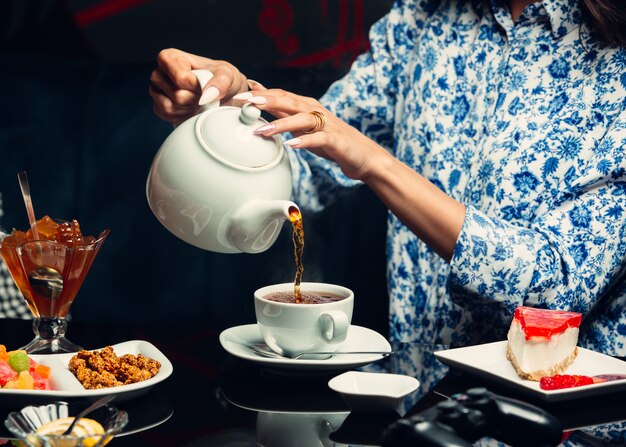 la donna versa il tè dalla teiera a una tazza bianca, cheesecake, marmellata