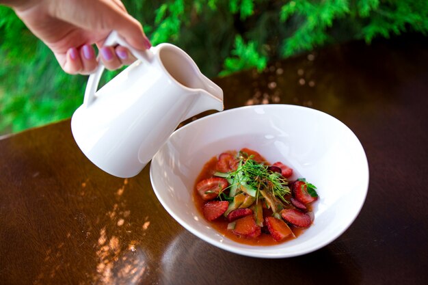 La donna versa la salsa nell'insalata della fragola e del cetriolo