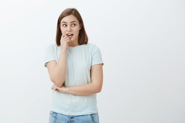 La donna vuole prendere i dolci esitando se la dieta lo consente. Incuriosita e curiosa donna carina eccitata e concentrata che si morde un'unghia mentre pensa guardando con desiderio