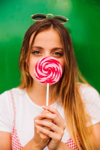 La faccia della donna che tiene il lecca-lecca rosso e rosa