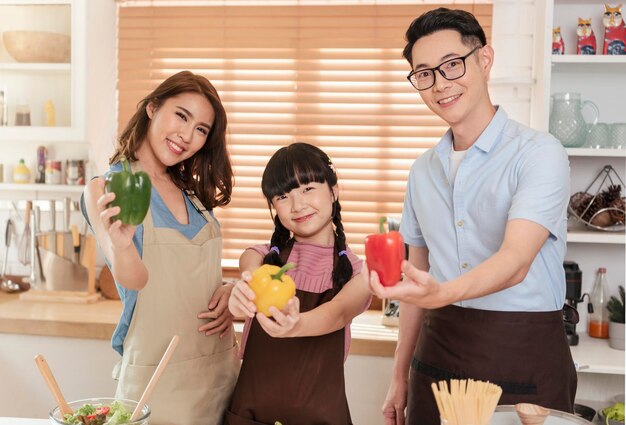 La famiglia asiatica si diverte a cucinare l'insalata e a mostrare il peperone insieme nella stanza della cucina a casa
