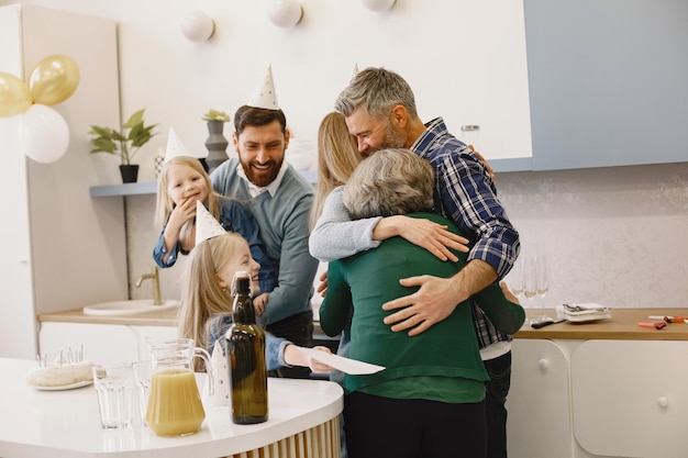 La famiglia e due delle loro figlie festeggiano il compleanno della nonna Figlio e figlia adulti che abbracciano sua madre