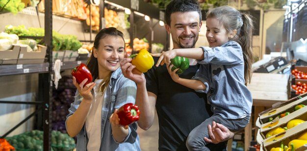 La famiglia felice compra verdure. Una famiglia di tre allegra che scelgono i pomodori nel dipartimento di verdure del supermercato o del mercato.