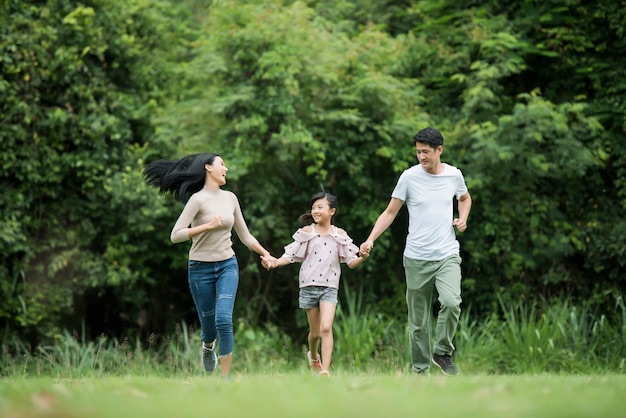 La famiglia felice si diverte Madre, padre e figlia stanno correndo nel parco.