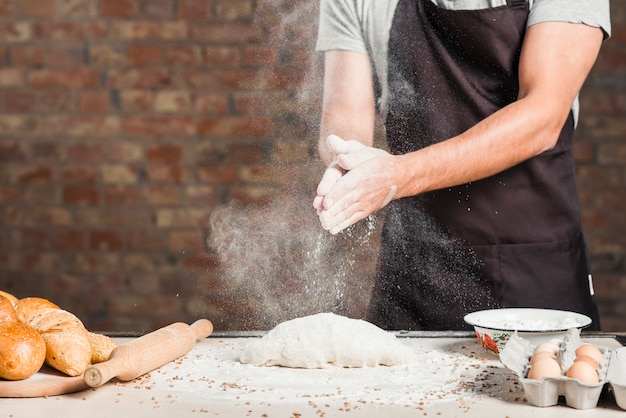 La farina per spolverare le mani del fornaio maschio sulla pasta impastata sopra il piano di lavoro della cucina