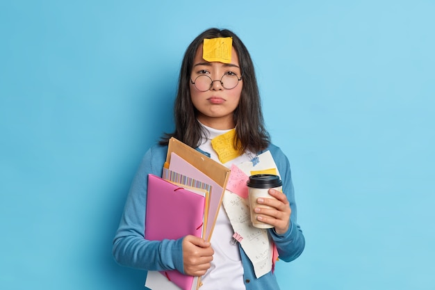 La fatica ha sottolineato la studentessa impegnata a preparare il rapporto o a lavorare sulla carta del diploma beve caffè per rinfrescarsi ha un adesivo con grafica attaccata sulla fronte stanca del lavoro.