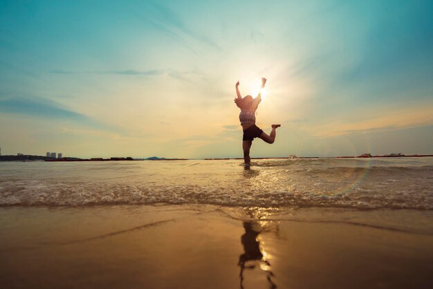 La felicità della bella donna asiatica di libertà salta e balla con lo sfondo della spiaggia al tramonto