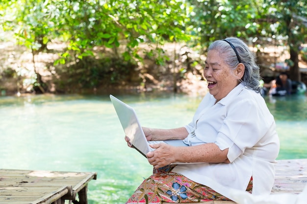 La femmina anziana asiatica gode di con il computer portatile
