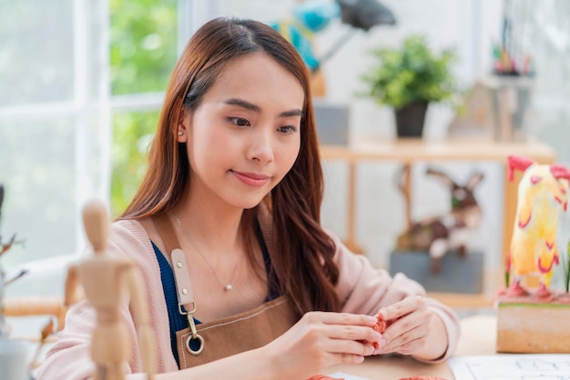 La femmina asiatica trascorre la giornata del fine settimana per il suo corso online di scultura di argilla hobby a casa giovane adulto che fa studio da corso di streaming su tablet online in costume da grembiule stile di vita casual asiatico a casa