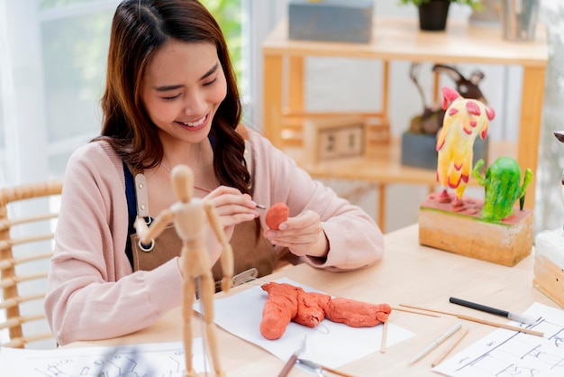 La femmina asiatica trascorre la giornata del fine settimana per il suo corso online di scultura di argilla hobby a casa giovane adulto che fa studio da corso di streaming su tablet online in costume da grembiule stile di vita casual asiatico a casa