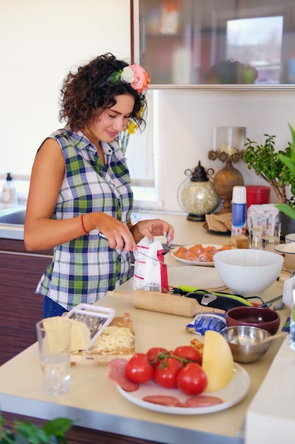 La femmina castana positiva fa la pasta in una cucina con i tulipani gialli sullo sfondo.