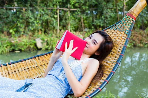 La femmina dell'adolescente che si trova sull'amaca di bambù e ha letto un libro