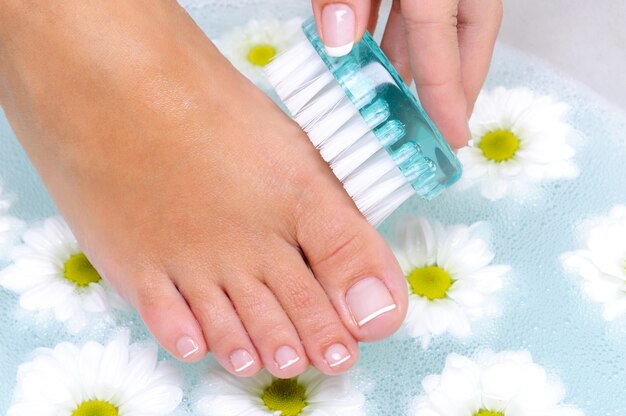 La femmina lava e pulisce le unghie dei piedi in acqua usando una spazzola