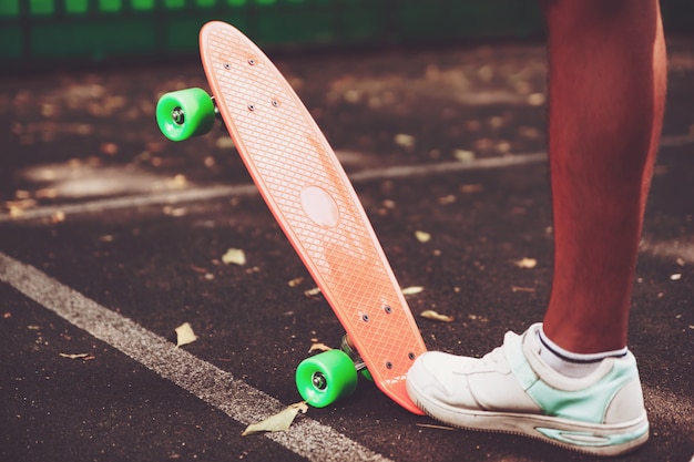 La fine dei piedi delle scarpe da tennis dell'uomo guida sul pattino arancio del penny su asfalto