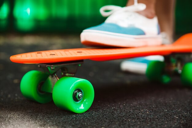 La fine dei piedi delle scarpe da tennis della ragazza guida sul pattino arancio del penny su asfalto